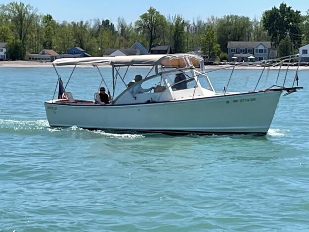1981 Dyer 29 Flush Deck/Bass Boat cruising on a sunny lake with trees in the background.