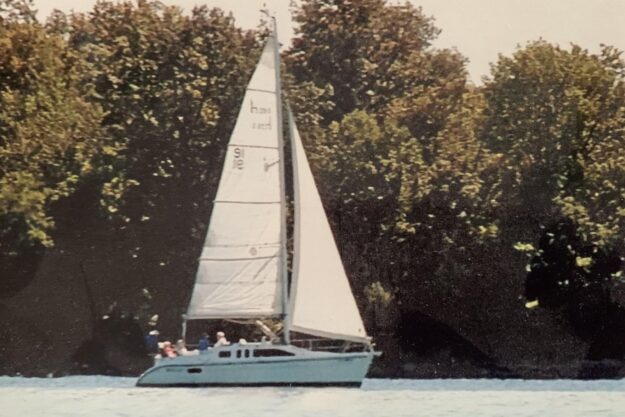 Sailboat Hunter 29.5 from 1994 sailing near a wooded shoreline.