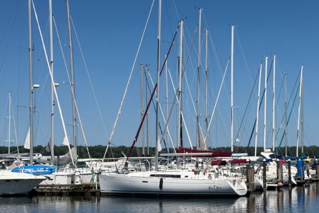 Sailboats docked at marina, featuring a 2012 Beneteau Oceanis 37 under clear blue sky.