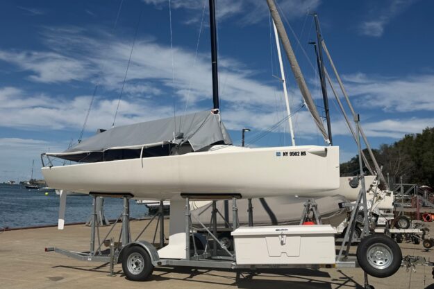 2023 J Boats J/70 sailboat on trailer by waterfront, under a clear blue sky.